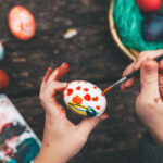 little girl painting easter egg on old wooden table